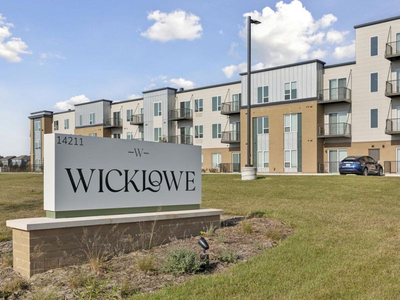 Sign reading "Wicklowe" in front of modern three-story apartment building on a sunny day.