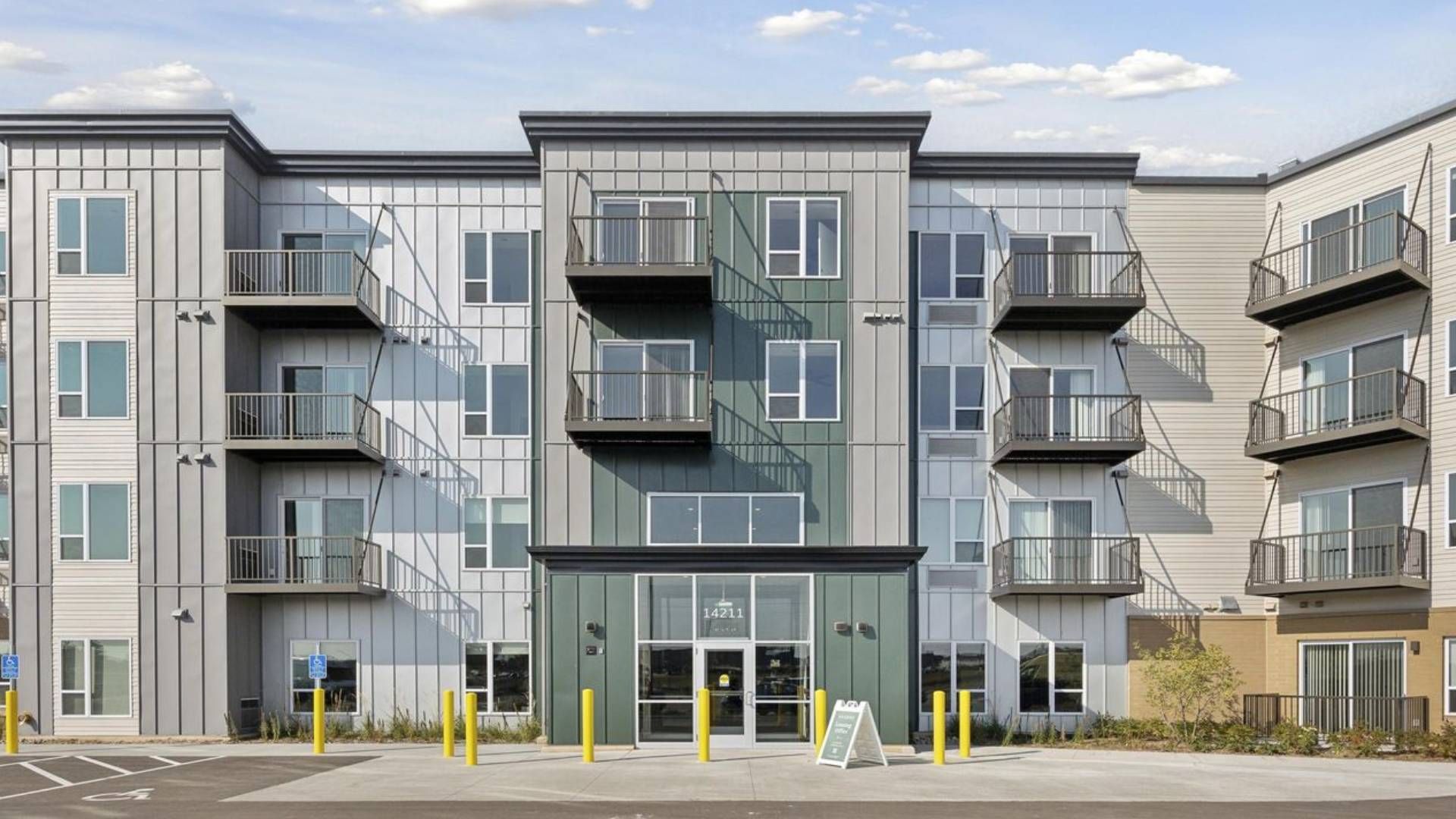 Modern four-story apartment building with balconies, large windows, and a main entrance at the center.