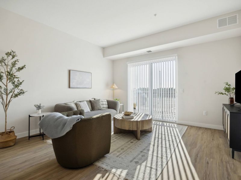 Modern living room with neutral decor, a gray sofa, armchair, TV, and sunlight streaming through vertical blinds.
