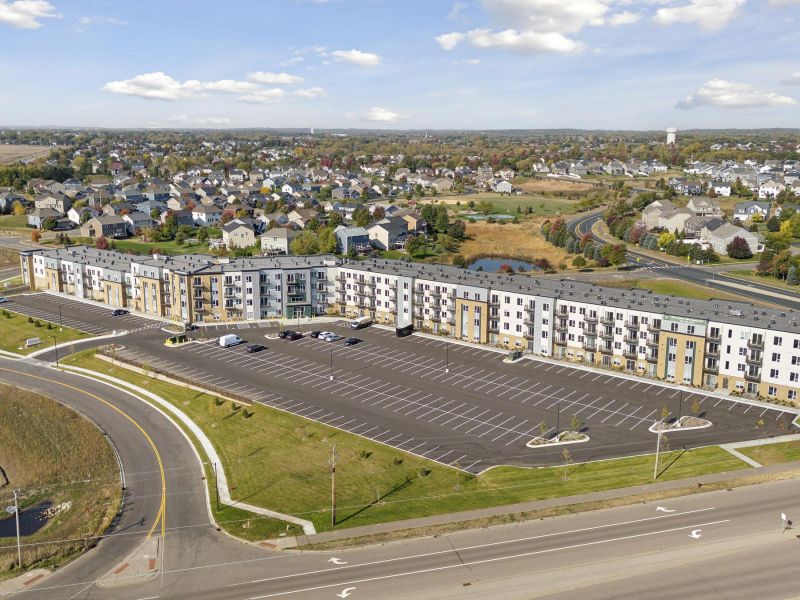 Aerial view of a large apartment building with a mostly empty parking lot in a suburban neighborhood.