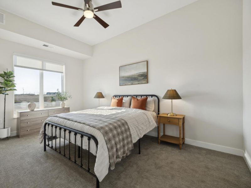Bright bedroom with a neatly made bed, two nightstands, lamps, a dresser, plant, and wall art.
