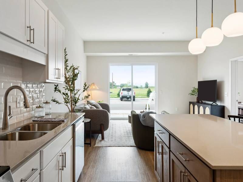 Modern open-plan kitchen and living room with neutral colors, large windows, and view of a car outside.