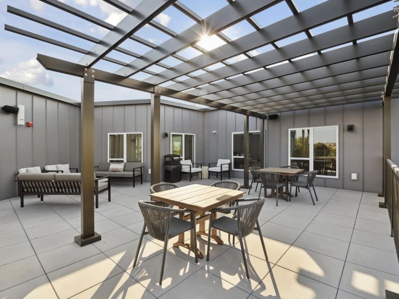 Modern rooftop patio with pergola, outdoor seating, and tables on a sunny day.