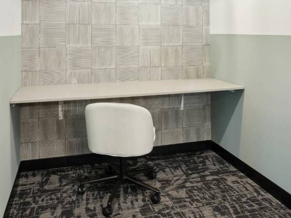 A white office chair faces an empty desk against a patterned wall in a small, modern workspace.