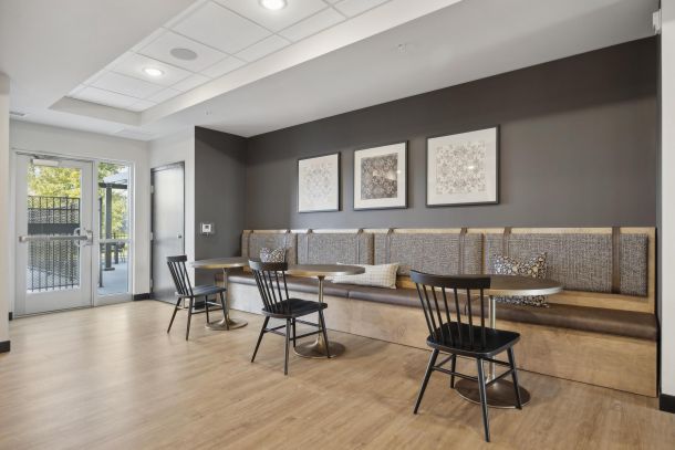Modern seating area with wooden tables, black chairs, wall art, and large windows letting in natural light.