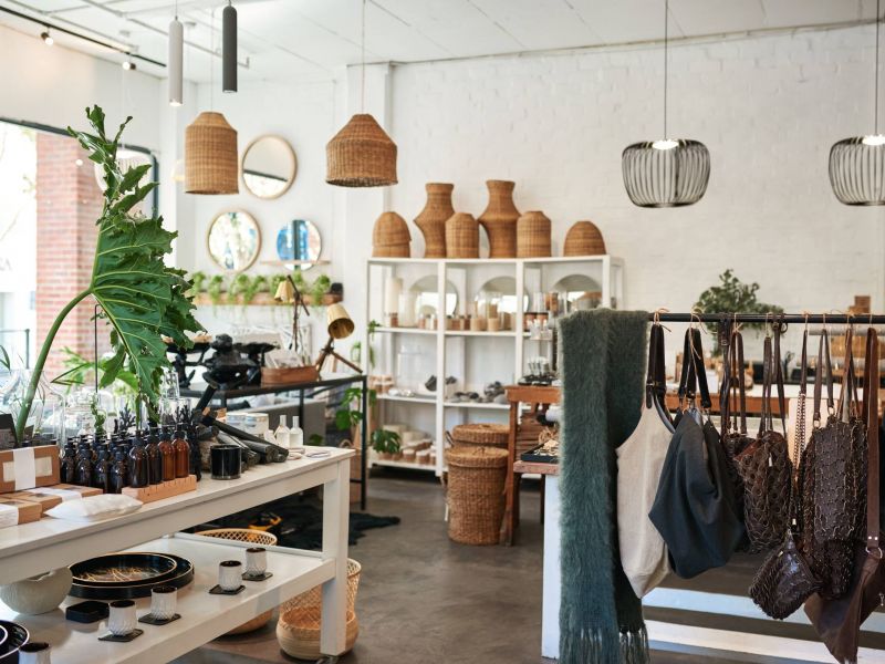 A modern boutique shop with shelves of home decor, baskets, plants, and hanging handbags.