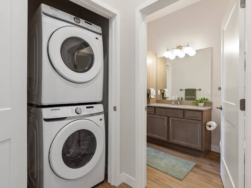 Stacked washer and dryer in a closet next to a modern bathroom with a vanity and mirror.