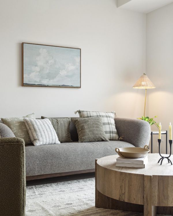 Modern living room with gray sofa, patterned pillows, round wooden coffee table, and wall art above the couch.
