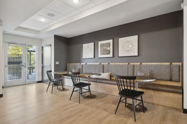 Modern seating area with wooden tables, black chairs, wall art, and large windows letting in natural light.